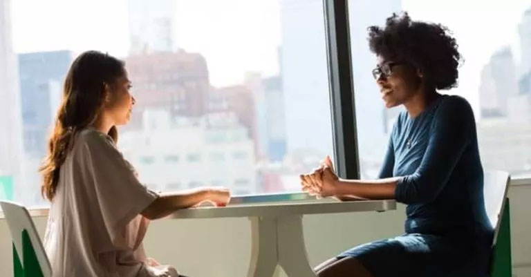 Two women sitting at a table by a window talking