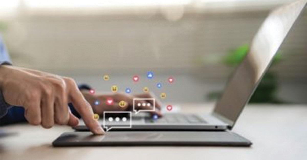 Person's hand typing on a laptop with emojis coming off the keyboard